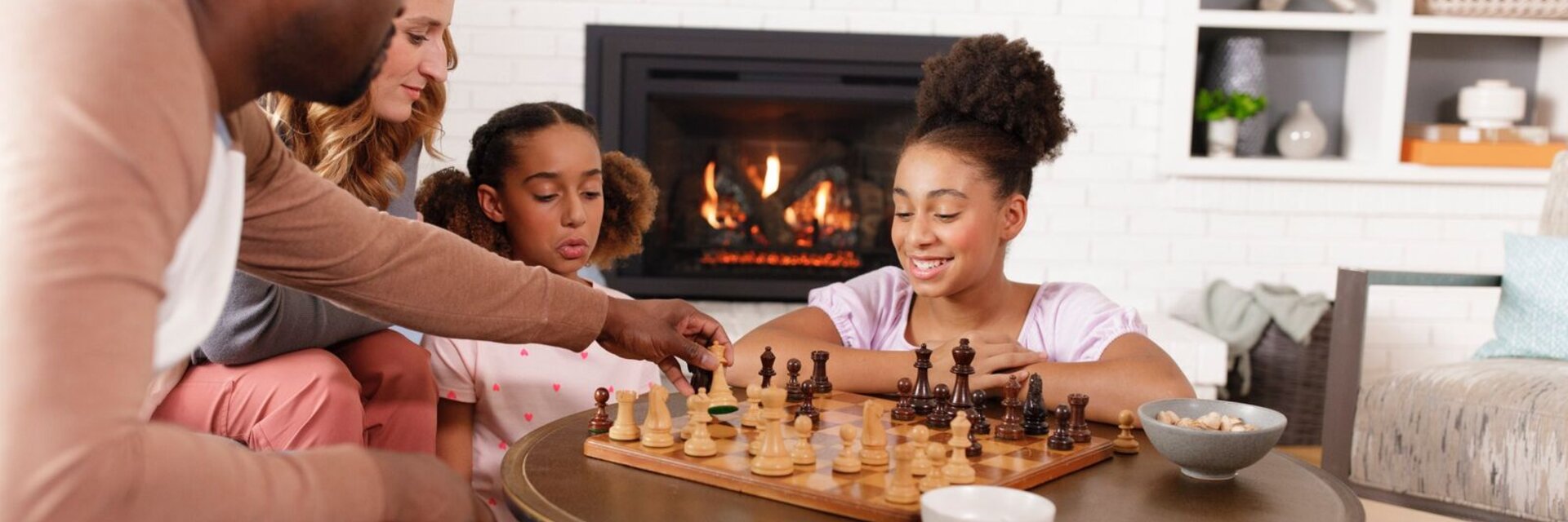 Family playing chess in front of a lit Heat & Glo fireplace