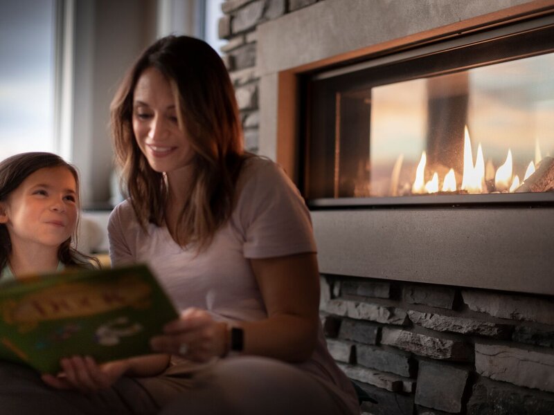 Mother and daughter reading a book in front of a lit linear gas fireplace